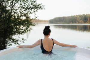 a woman relaxing in an outdoor hot tub overlooking a lake
