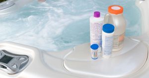 Hot tub maintenance accessories including a spa vacuum, chemical dispenser, and filter cleaner on a deck.